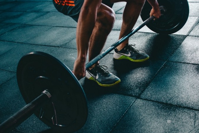 Person crouched gripping a barbell with weight plates on a rubber gym floor