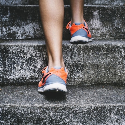 Person in orange running shoes climbing moss-covered concrete stairs outdoors